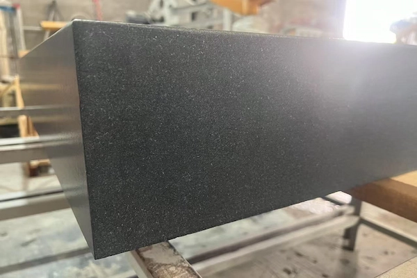 Textured black granite plinth edge shown during a dimensional check in a supplied factory image