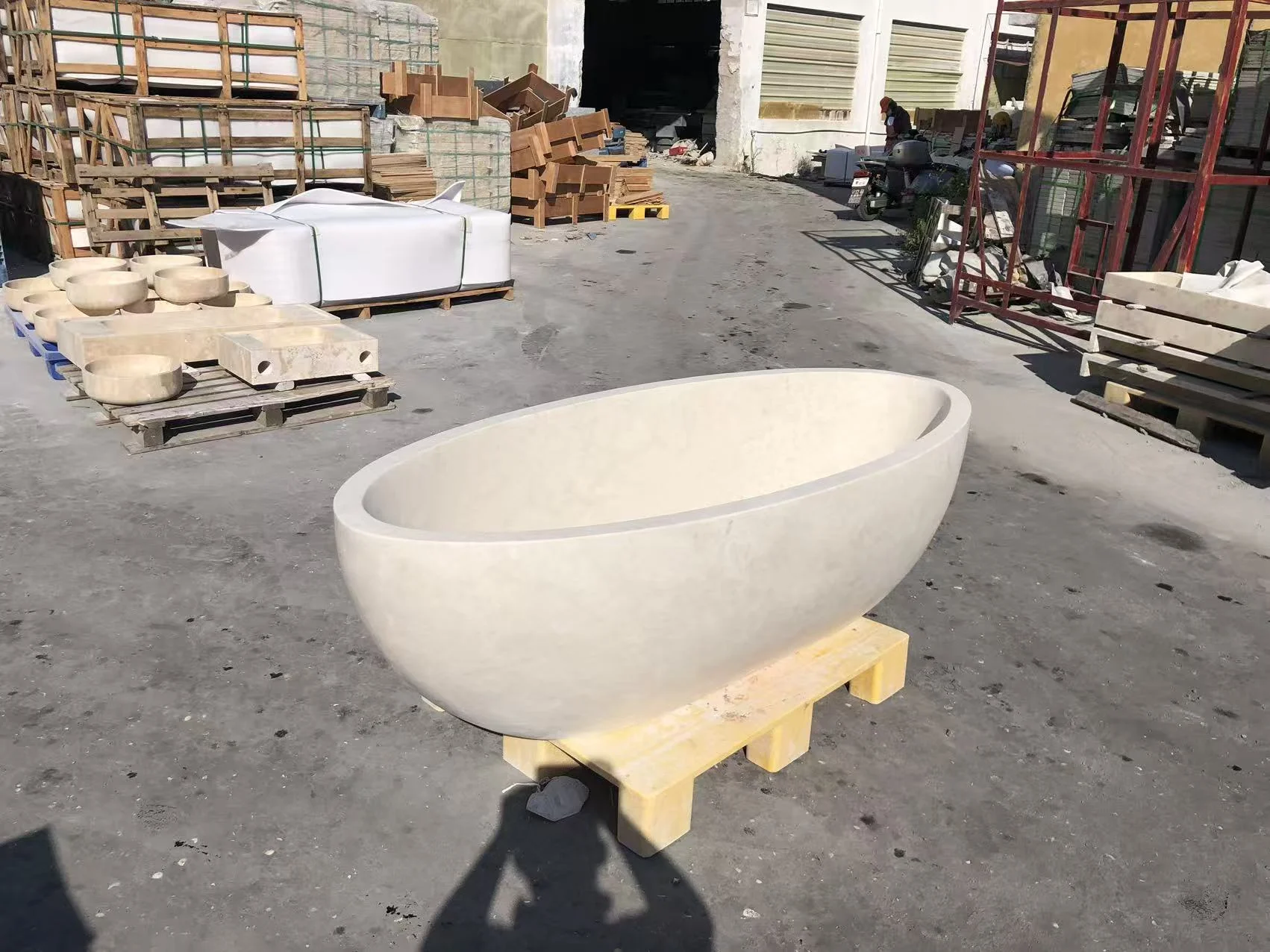 Oval beige limestone bathtub prepared on a support base in a factory yard