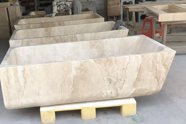 Rectangular beige limestone bathtub in a factory workshop with additional stone bath forms in the background