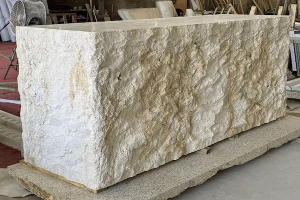 Beige limestone reception desk with a split-face front panel and smooth counter surface shown on a workshop support base