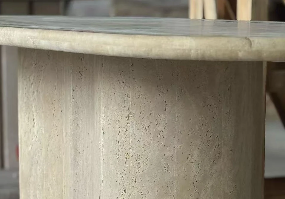 Close-up of an oval beige travertine tabletop edge during surface and joint inspection