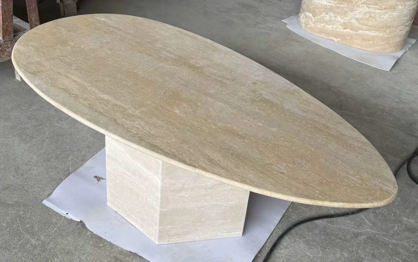 Beige travertine oval table top and geometric pedestal components shown during production inspection