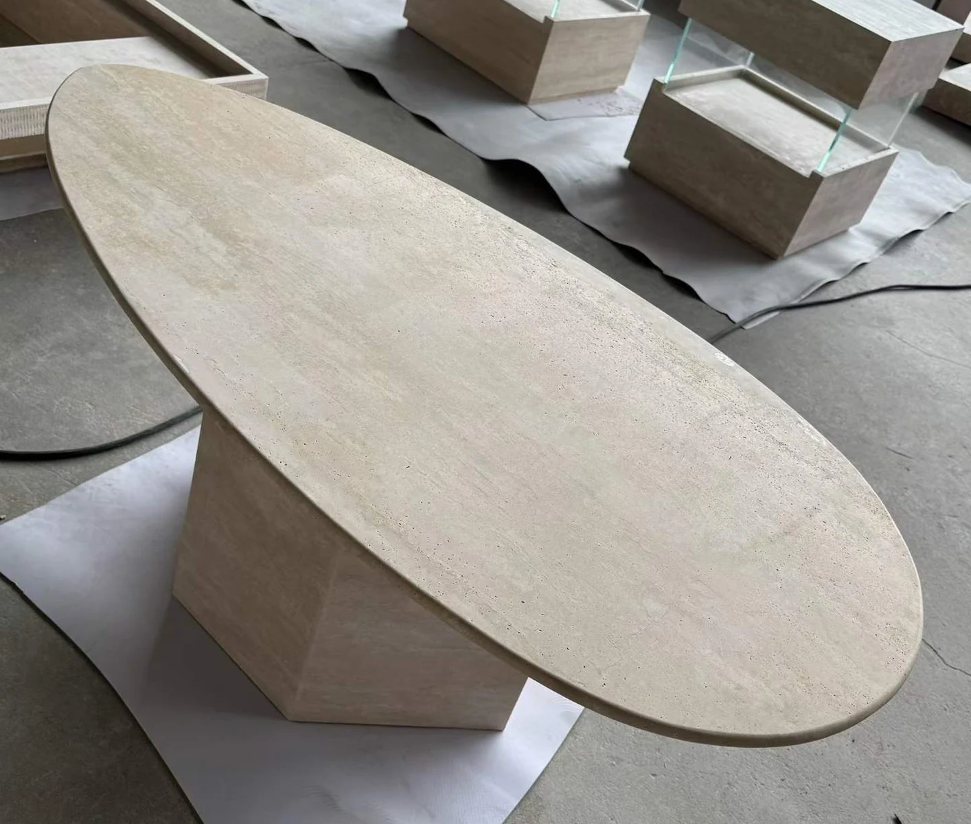Low oval travertine coffee table assembled with a geometric pedestal in a stone workshop