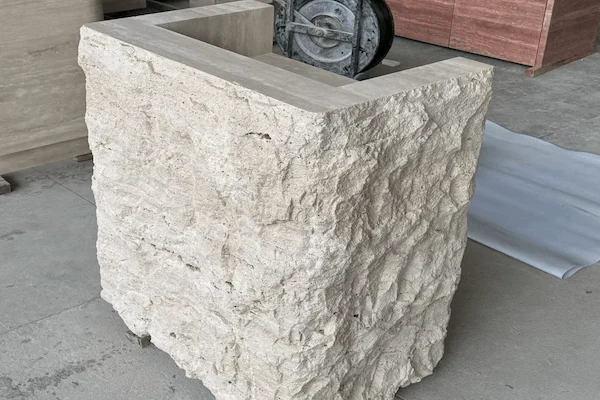 Beige travertine reception desk with a textured stone front and smooth counter profile shown in the workshop