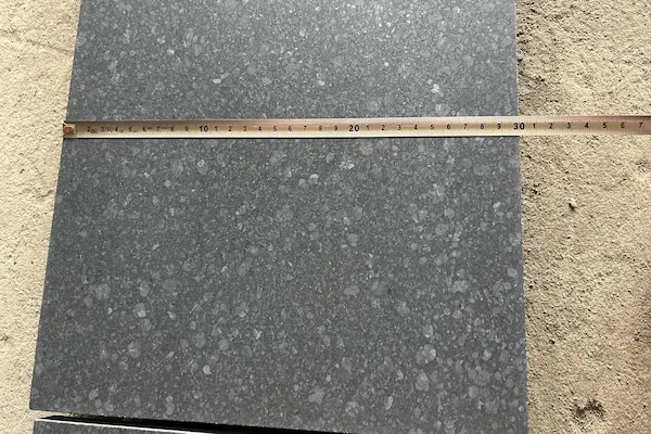 Honed G684 Black Basalt tile with a straightedge in a supplied production quality-check image