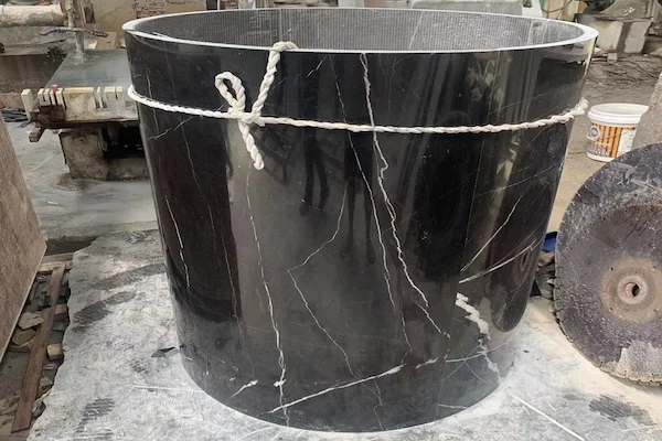 Cylindrical Black Marble column component with pale linear veining in a stone workshop