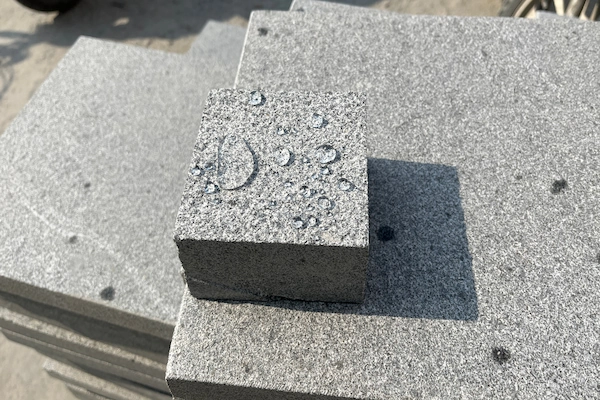 Classic Grey Granite cube stone with water beading on its light-grey textured surface during inspection