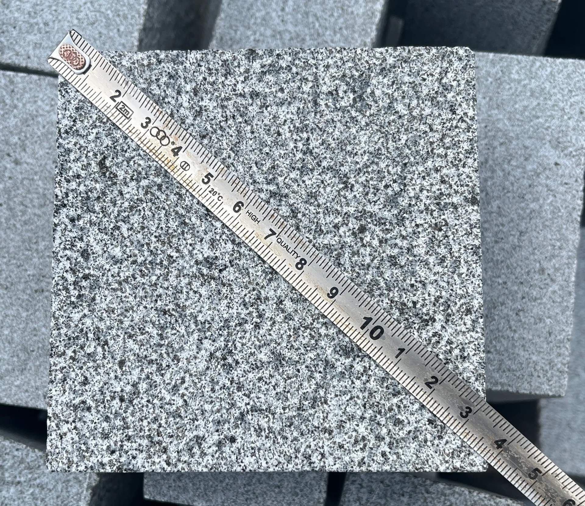 Measuring tape checking the width of a cut Classic Grey Granite paving piece during dimensional quality control