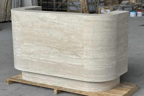 Curved beige travertine reception desk on a workshop base showing the rounded stone front
