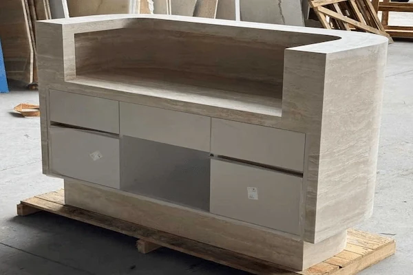 Staff-side view of a curved beige travertine reception desk showing an internal carcase during workshop review