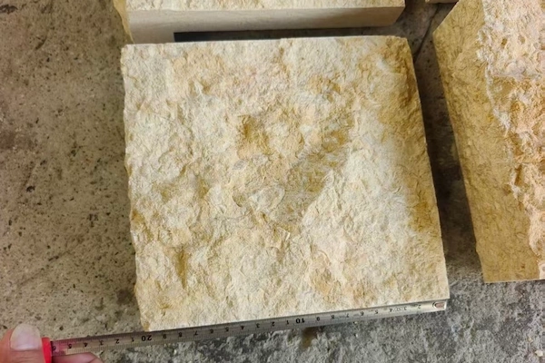 Supplied close-up reference of a beige Rock Face Limestone cladding piece with a tape measure for format review