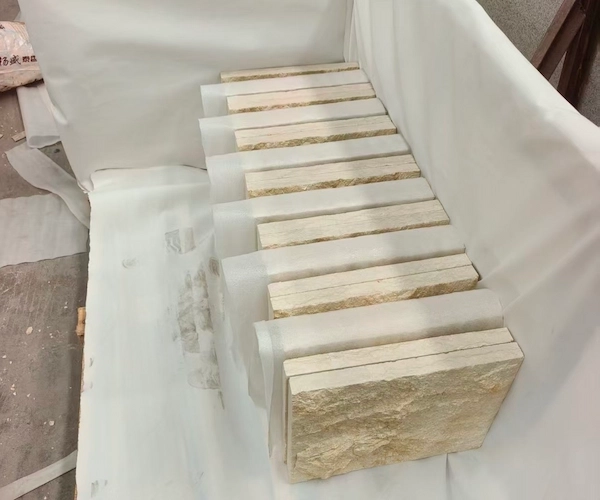 Supplied reference of beige Rock Face Limestone cladding pieces stacked on protective sheets for handling discussion
