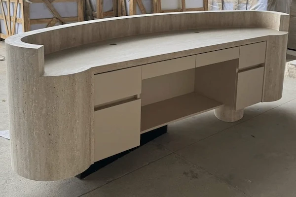 Staff-side view of a beige travertine reception desk showing fitted cabinets and a broad worktop