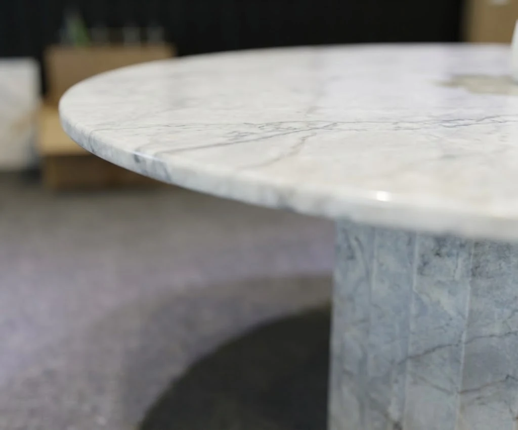 Close-up of a rounded white marble coffee table edge and fluted pedestal surface during finishing review