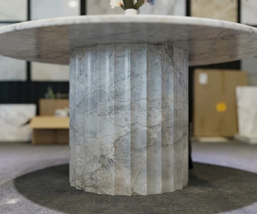 White marble fluted pedestal beneath a round tabletop shown during furniture production inspection